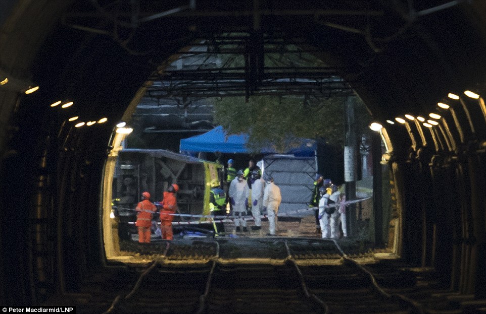 Emergency workers inspect the derailed tram as darkness falls in Croydon this evening. At least seven people died in the crash and 50 passengers were injured